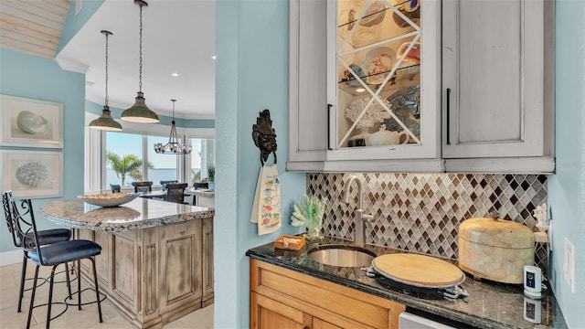 kitchen with a kitchen breakfast bar, dark stone countertops, hanging light fixtures, decorative backsplash, and sink