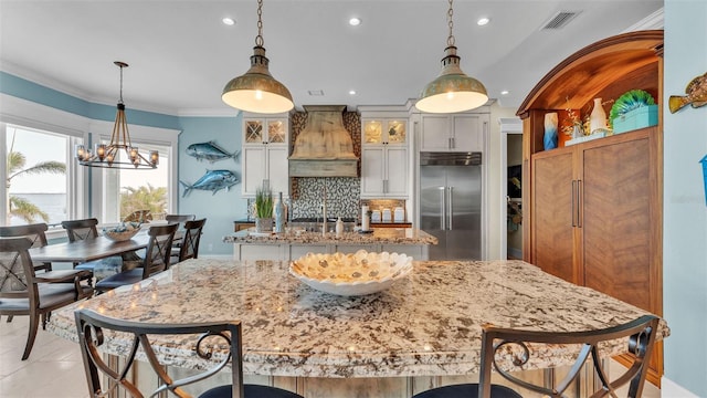 kitchen featuring built in fridge, premium range hood, light stone counters, decorative backsplash, and white cabinets