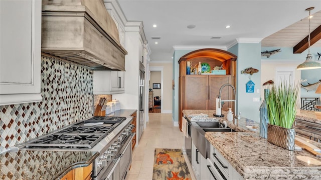 kitchen featuring light stone countertops, premium range hood, decorative backsplash, white cabinets, and sink