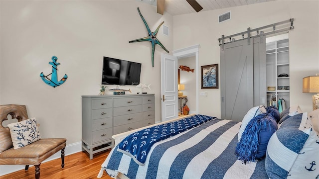 bedroom featuring vaulted ceiling, a barn door, a closet, ceiling fan, and light hardwood / wood-style flooring