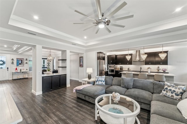 living room with sink, a raised ceiling, dark hardwood / wood-style flooring, crown molding, and ceiling fan with notable chandelier