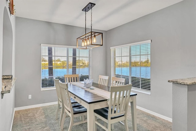 carpeted dining room with plenty of natural light, a water view, and a notable chandelier