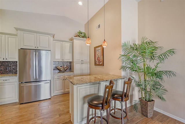 kitchen featuring stainless steel refrigerator, light stone countertops, pendant lighting, vaulted ceiling, and decorative backsplash