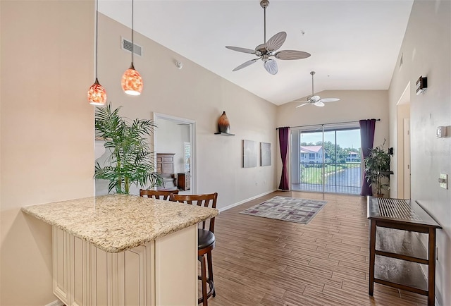 kitchen featuring hanging light fixtures, cream cabinets, vaulted ceiling, a breakfast bar, and hardwood / wood-style flooring