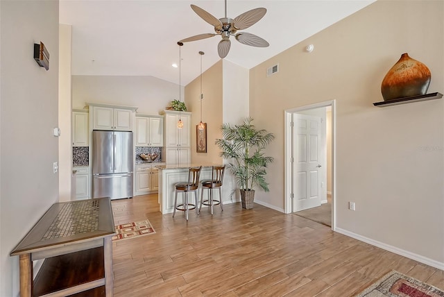 kitchen with a kitchen bar, stainless steel fridge, backsplash, vaulted ceiling, and ceiling fan