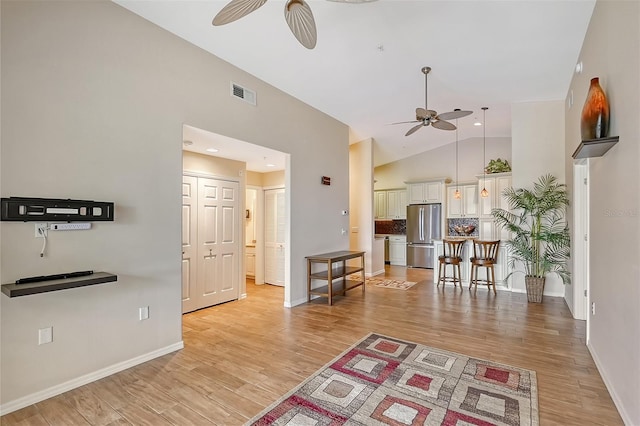 living room with ceiling fan, vaulted ceiling, and light wood-type flooring