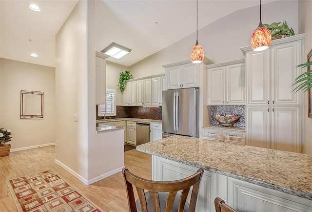 kitchen with lofted ceiling, white cabinetry, light stone counters, decorative light fixtures, and appliances with stainless steel finishes