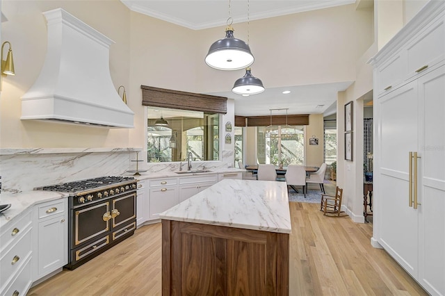 kitchen with sink, white cabinetry, light stone countertops, custom range hood, and range with two ovens