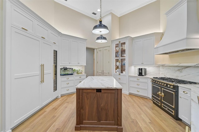 kitchen featuring custom exhaust hood, hanging light fixtures, light stone countertops, range with two ovens, and white cabinets