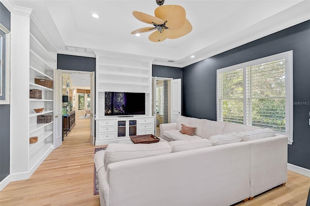 living room with crown molding, a tray ceiling, light hardwood / wood-style floors, and built in shelves