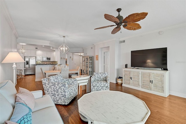 living room featuring ceiling fan with notable chandelier, dark wood-type flooring, and ornamental molding