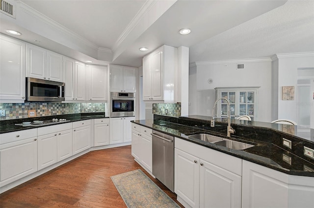 kitchen with sink, dark stone countertops, white cabinets, stainless steel appliances, and light wood-type flooring