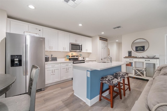 kitchen with white cabinetry, stainless steel appliances, a kitchen bar, and a center island with sink