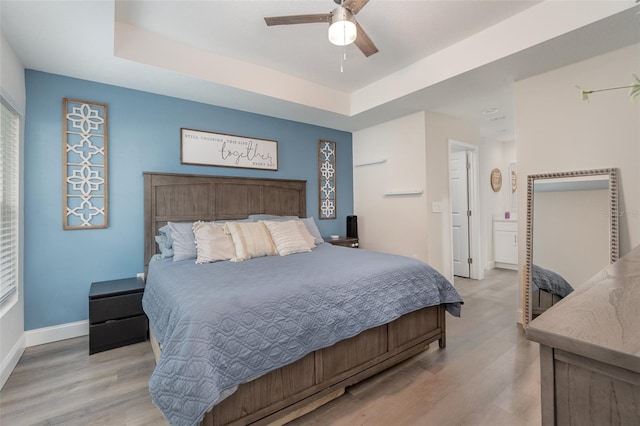 bedroom featuring ceiling fan, light wood-type flooring, and a tray ceiling