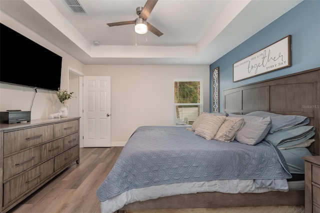 bedroom with ceiling fan, light hardwood / wood-style flooring, and a tray ceiling