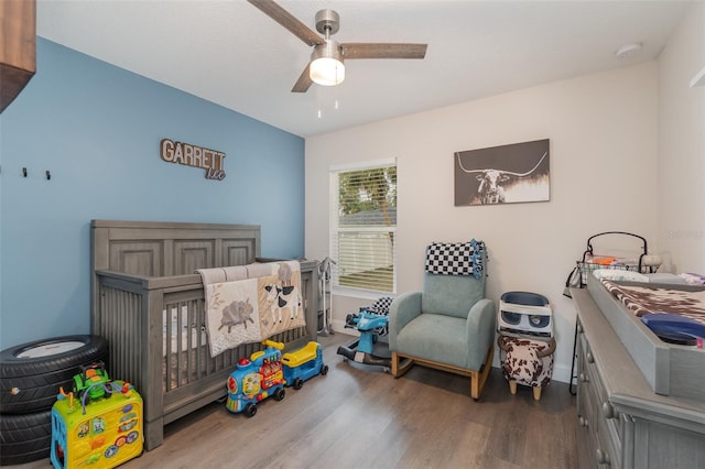 bedroom featuring ceiling fan, wood-type flooring, and a crib