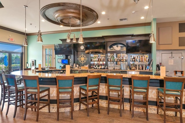 bar featuring hardwood / wood-style floors, ornamental molding, and hanging light fixtures