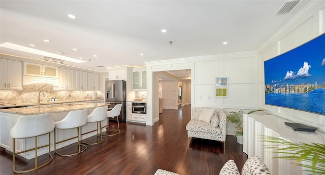 kitchen with light stone countertops, high end refrigerator, ornamental molding, white cabinets, and oven