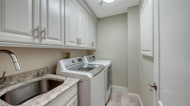 clothes washing area with washing machine and clothes dryer, cabinets, and sink