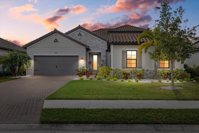 mediterranean / spanish-style house featuring decorative driveway, stone siding, a garage, and stucco siding