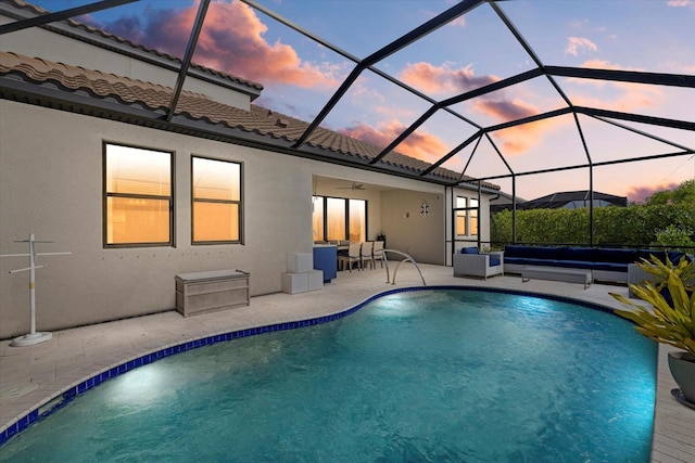 pool at dusk with glass enclosure, a patio area, and an outdoor hangout area