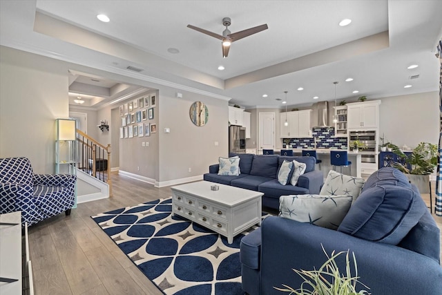 living room featuring ceiling fan, light wood-type flooring, and a tray ceiling