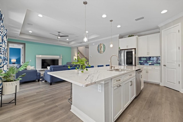 kitchen featuring a center island with sink, white cabinetry, stainless steel appliances, and hanging light fixtures