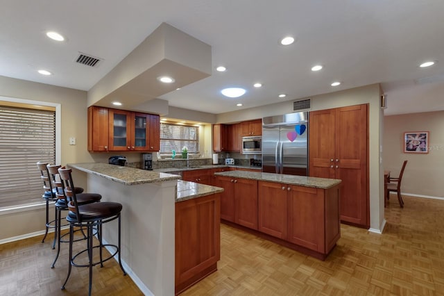 kitchen with a breakfast bar, sink, built in appliances, light parquet floors, and light stone counters