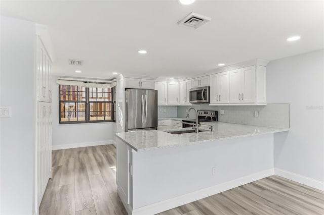 kitchen with light stone countertops, kitchen peninsula, appliances with stainless steel finishes, and white cabinetry