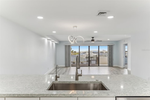 kitchen featuring sink, ceiling fan with notable chandelier, light stone counters, and decorative light fixtures