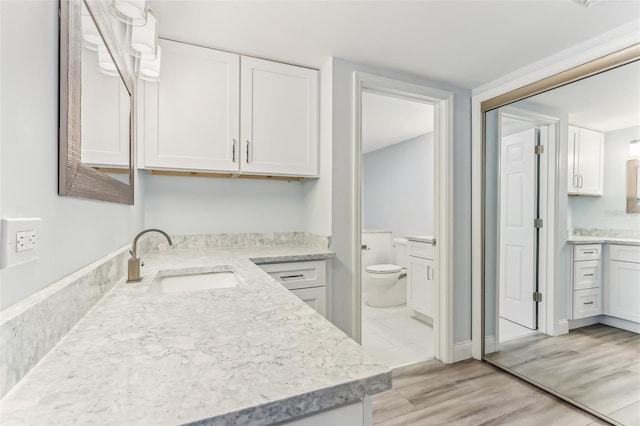 kitchen featuring white cabinets, sink, light stone counters, and light hardwood / wood-style flooring