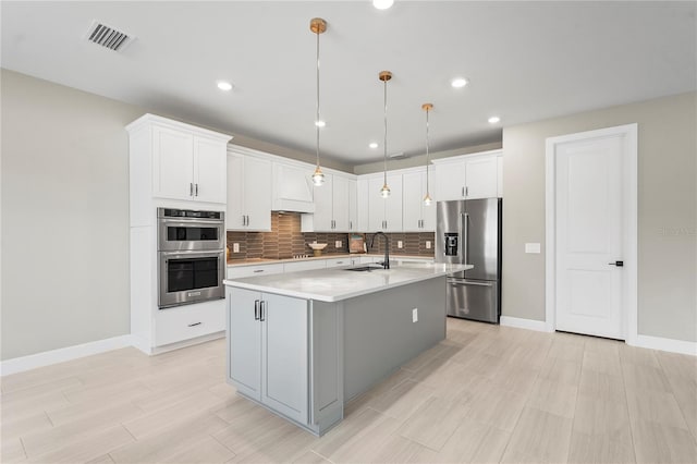 kitchen featuring an island with sink, white cabinetry, sink, hanging light fixtures, and stainless steel appliances