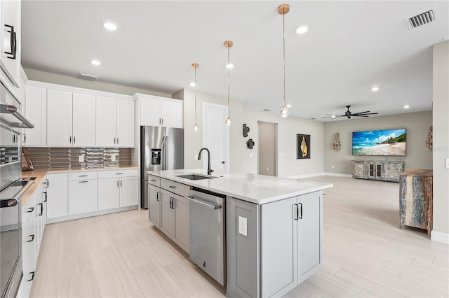 kitchen featuring sink, a center island with sink, pendant lighting, stainless steel appliances, and white cabinets