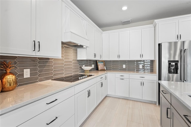 kitchen featuring high end refrigerator, backsplash, white cabinets, light stone counters, and black electric cooktop