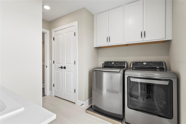 laundry area featuring cabinets, washer and dryer, and light hardwood / wood-style flooring