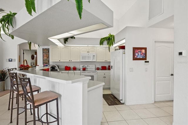 kitchen with light tile patterned floors, white appliances, a breakfast bar, decorative backsplash, and kitchen peninsula