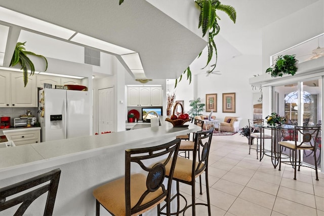 kitchen featuring light tile patterned flooring, white cabinetry, white refrigerator with ice dispenser, and backsplash