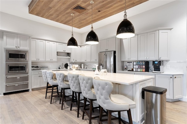 kitchen with wood ceiling, light hardwood / wood-style floors, stainless steel appliances, decorative light fixtures, and a kitchen island with sink