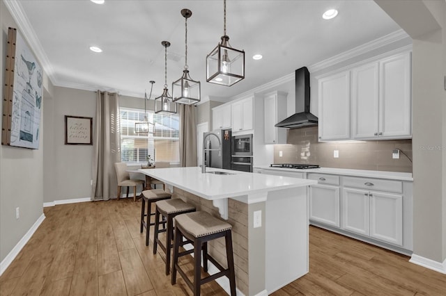 kitchen featuring pendant lighting, white cabinets, wall chimney range hood, and an island with sink