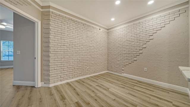 empty room featuring crown molding, light wood-type flooring, and brick wall