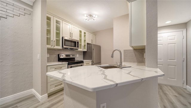 kitchen featuring light stone countertops, sink, white cabinets, kitchen peninsula, and stainless steel appliances