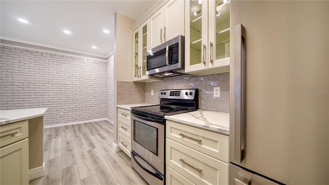 kitchen featuring light stone countertops, brick wall, appliances with stainless steel finishes, and light wood-type flooring