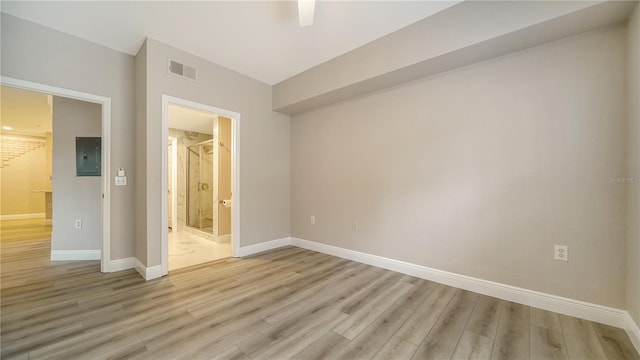 unfurnished bedroom with ceiling fan, light hardwood / wood-style flooring, connected bathroom, and electric panel