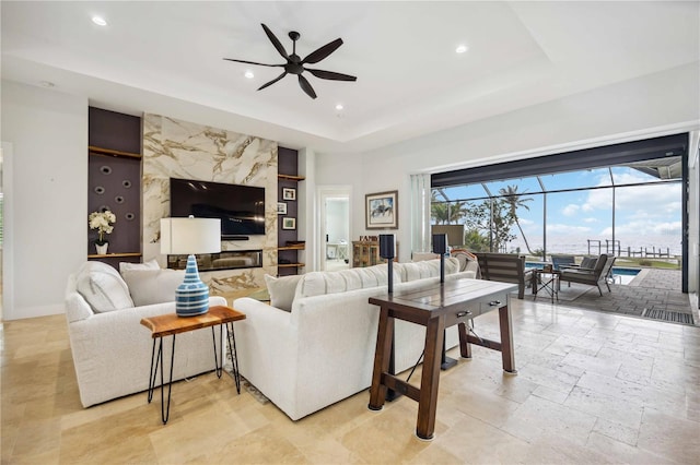 living room with a fireplace, ceiling fan, and a tray ceiling