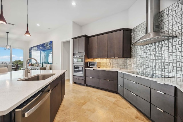 kitchen featuring appliances with stainless steel finishes, wall chimney range hood, decorative backsplash, sink, and decorative light fixtures