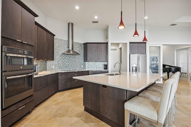 kitchen with a kitchen island with sink, stainless steel appliances, wall chimney exhaust hood, sink, and tasteful backsplash