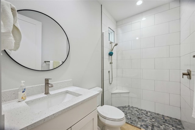 bathroom featuring toilet, tiled shower, and vanity