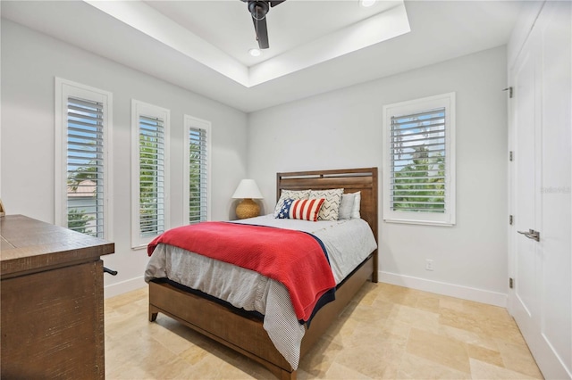 bedroom with ceiling fan, multiple windows, and a tray ceiling