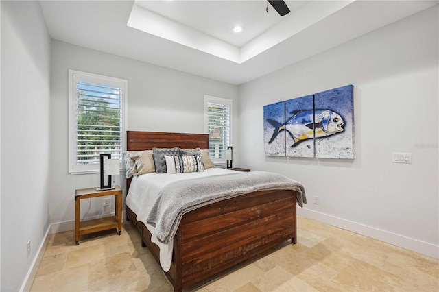 bedroom with ceiling fan, multiple windows, and a tray ceiling