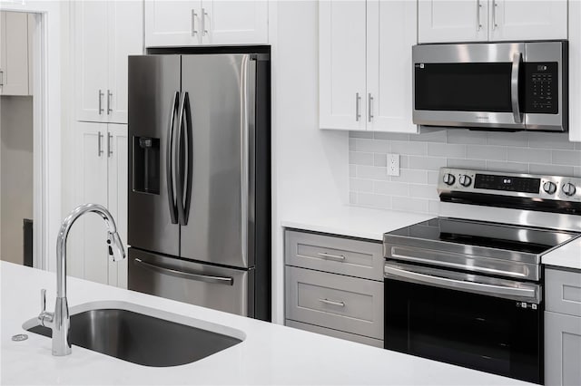 kitchen with stainless steel appliances, white cabinetry, sink, and backsplash